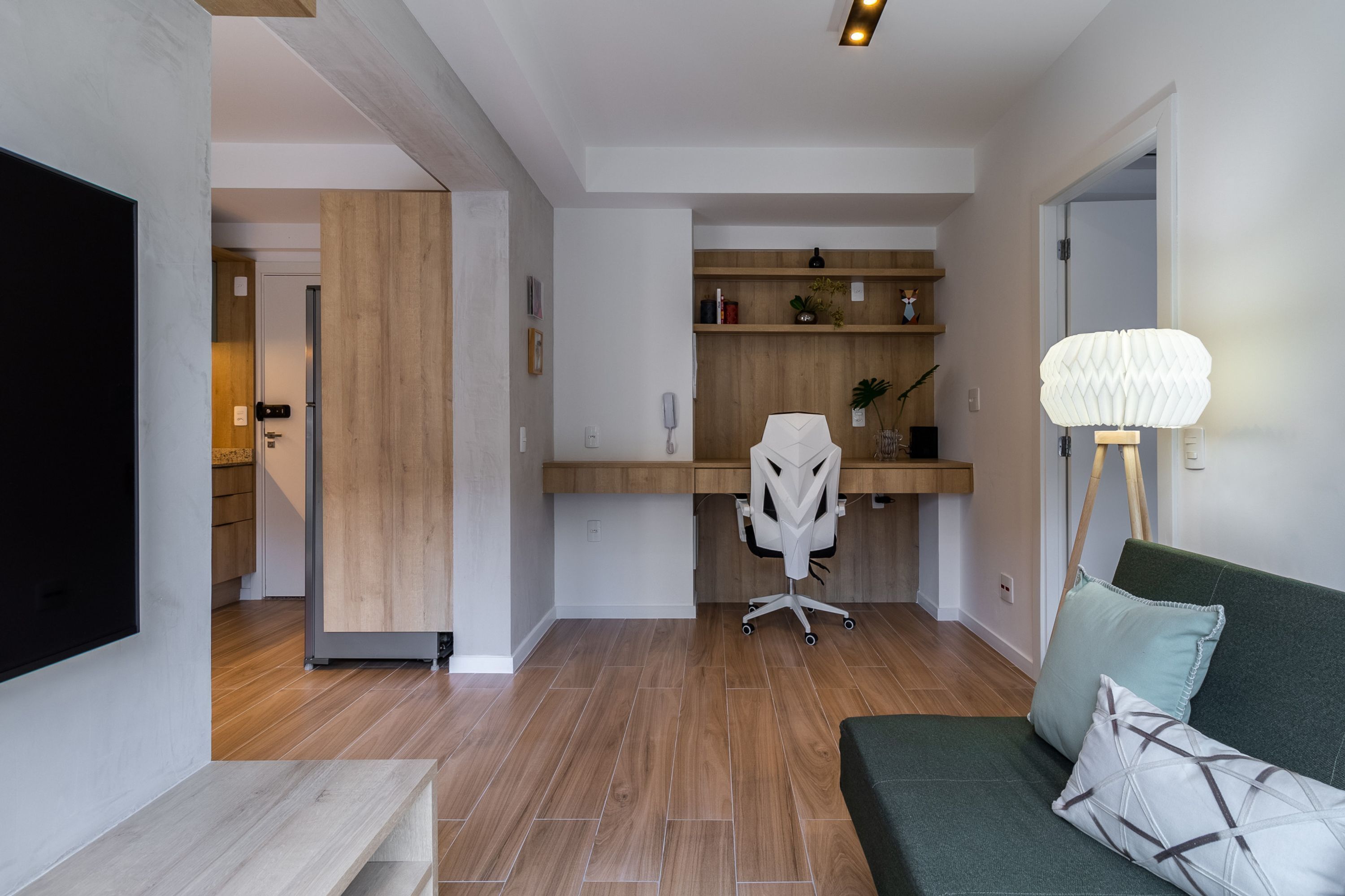 Ein modernes Wohnzimmer mit einem grünen Sofa, einem weißen Bürostuhl, einem Holztisch und einer Lampe.