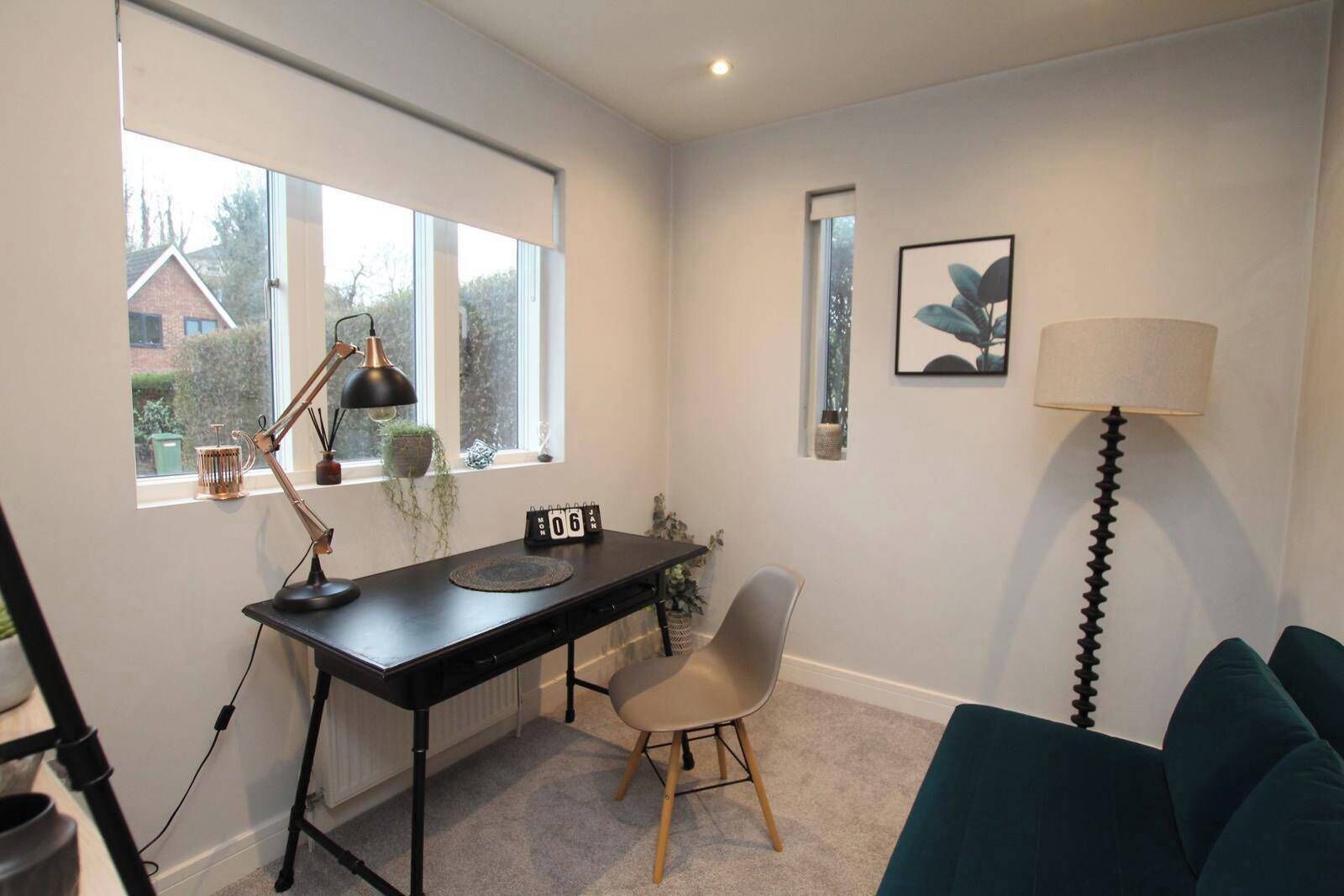 A room with a desk, chair, and a couch. There is a window with a view of houses outside.