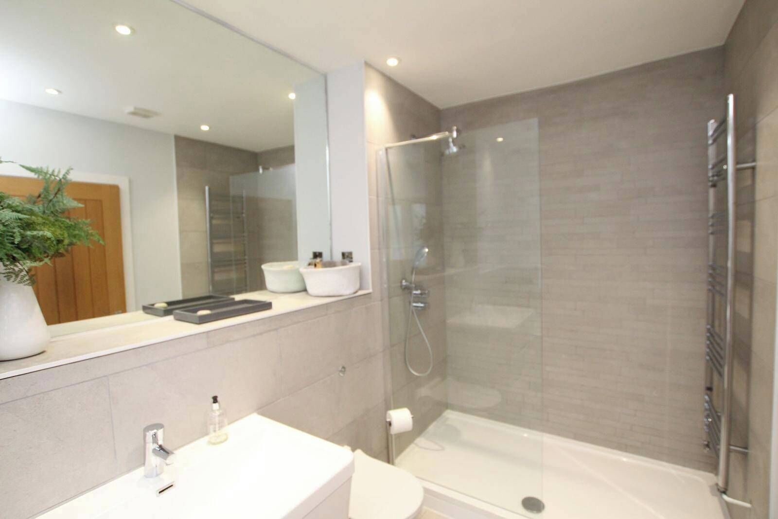 A modern bathroom with a glass-enclosed shower, a white sink, and a large mirror.