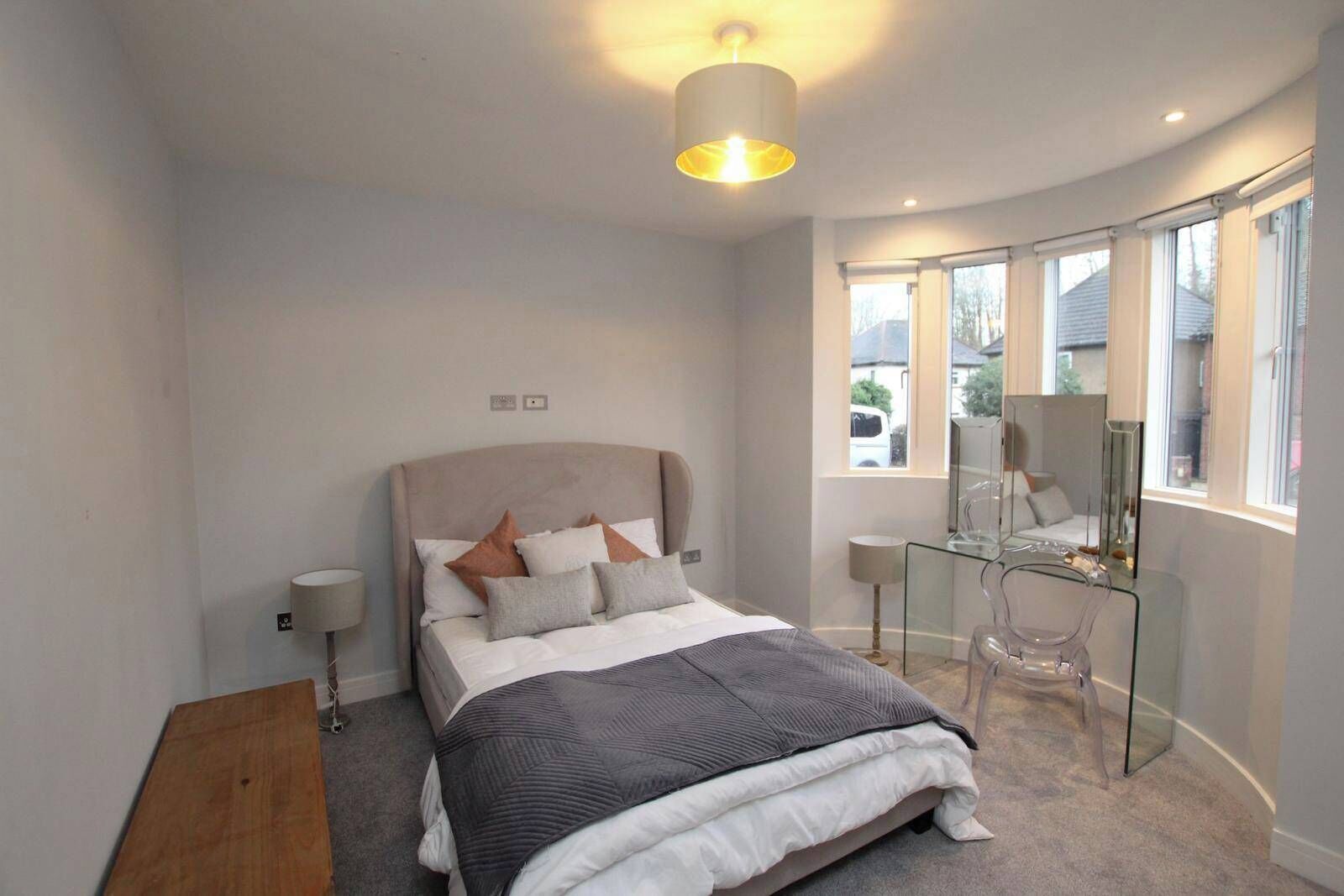 Un dormitorio moderno con cama, lámparas de noche, un escritorio de cristal y un ventanal grande.