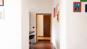 A narrow hallway with a wooden door at the end, a dining area with a table and stools, and several framed artworks on the walls. - Casa Fiamma in Rome With 1 Bedrooms and 1 Bathrooms (Rome)