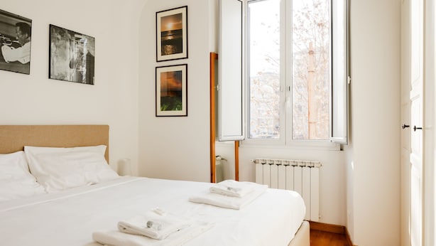 A neatly made bed with white linens and towels, a window with a view of trees, and three framed pictures on the wall. - Casa Fiamma in Rome With 1 Bedrooms and 1 Bathrooms (Rome)