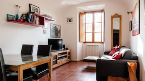 A living room with a glass-top dining table, black chairs, a sofa, a TV on a wooden cabinet, a bookshelf, and a window with a wooden shutter. - Casa Fiamma in Rome With 1 Bedrooms and 1 Bathrooms (Rome)