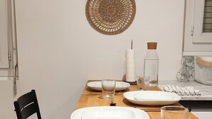 Uma sala de jantar com uma mesa de madeira posta para dois, uma cadeira preta e duas tapeçarias de parede.