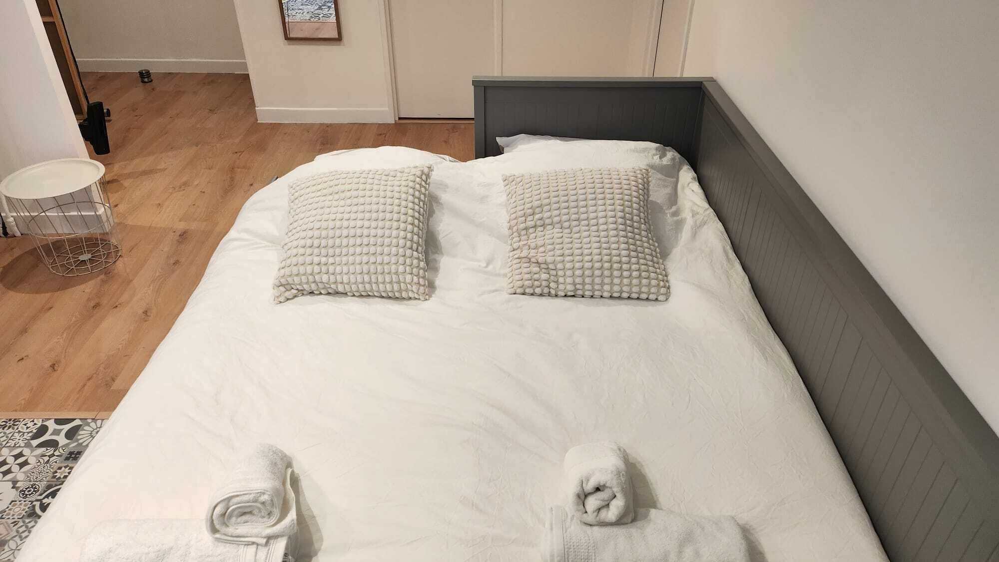 Een keurig opgemaakt bed met twee kussens en twee opgerolde handdoeken aan het voeteneinde.