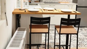 Uma cozinha moderna com armários brancos, painel de fundo de mármore e uma ilha central com cadeiras.