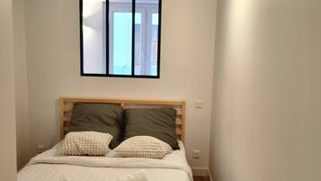 Une chambre à coucher avec un lit, des oreillers, une fenêtre et un luminaire fixé au mur.