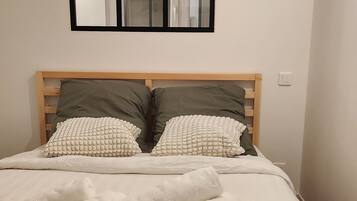 Ein ordentlich gemachtes Bett mit weißen Leinentüchern und aufgerollten Handtüchern, ein Holz-Kopfteil und ein Spiegel darüber.