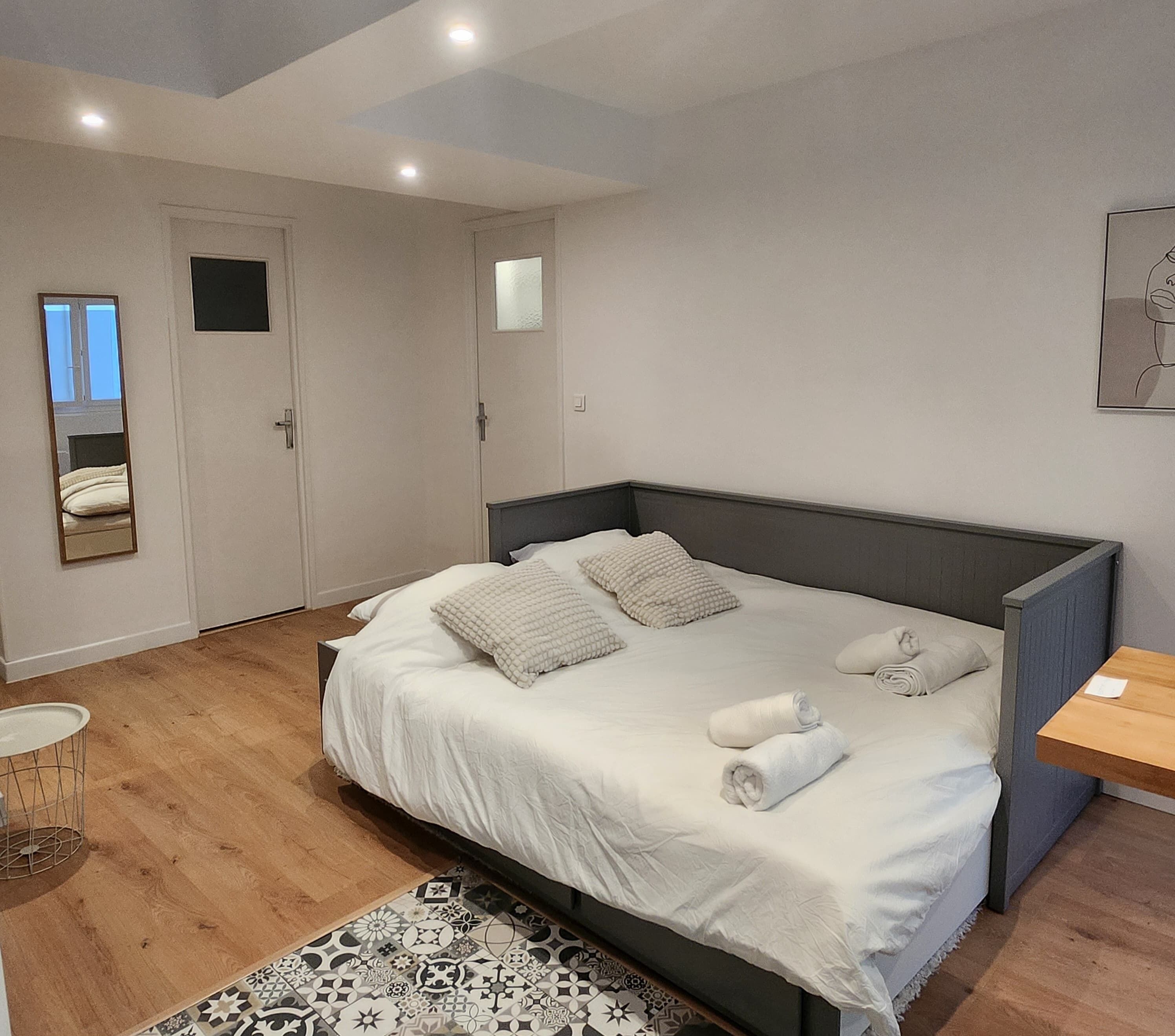 Une chambre à coucher moderne avec un grand lit, une table de chevet, un miroir et une petite table ronde.