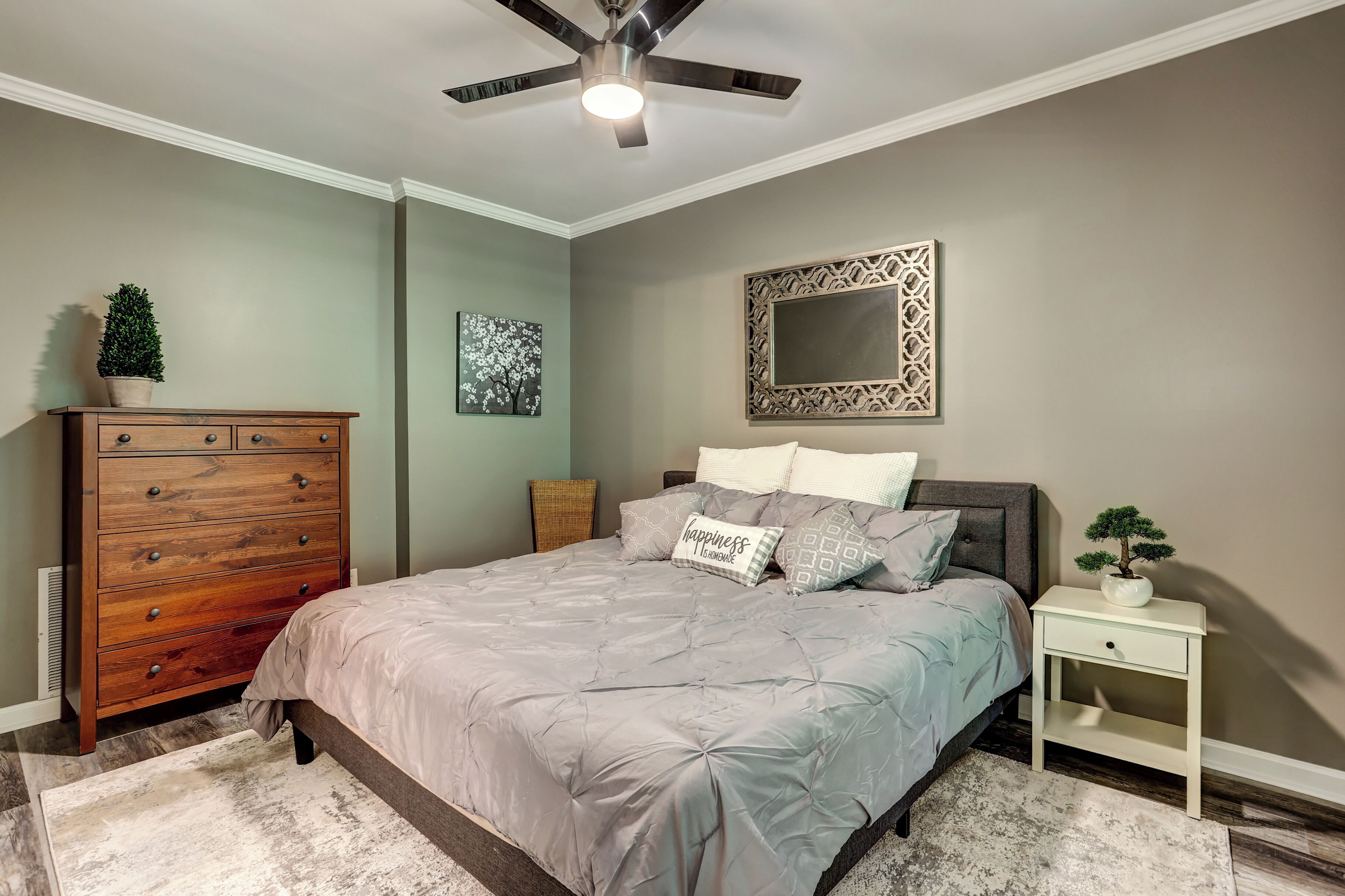 Un dormitorio con cama, cómoda, mesita de noche, ventilador de techo y decoración en la pared.