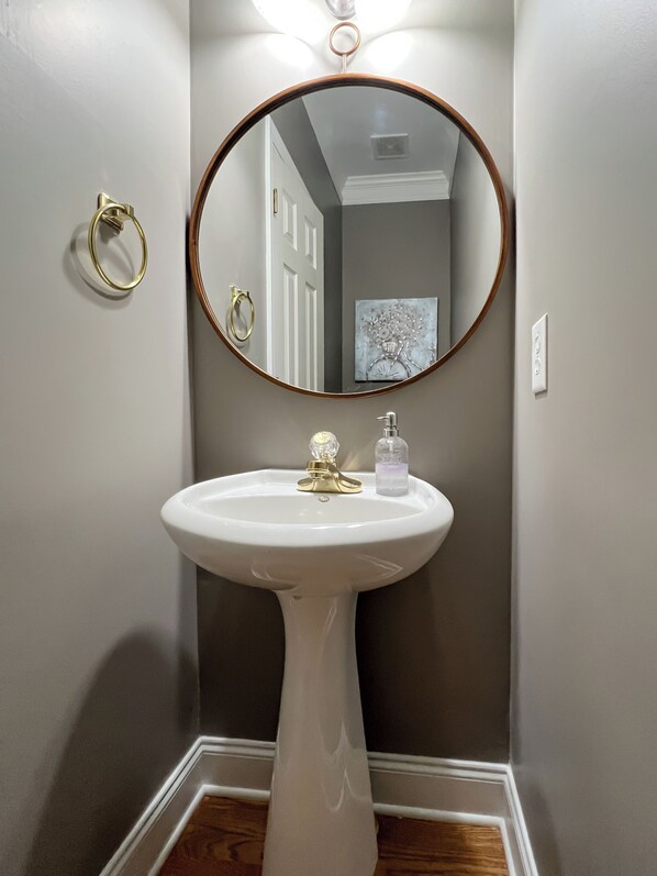 A bathroom with a pedestal sink, a round mirror, and a gold towel ring.