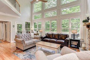A spacious living room with a high ceiling, large windows, a fireplace, and a cozy seating area.