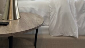 Een moderne slaapkamer met een ronde houten tafel, een metalen lamp en een bed met wit beddengoed.