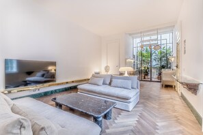 A modern living room with a large flat-screen TV, a grey sofa, a coffee table, and a herringbone-patterned floor. - EVA Loft - Studio Apartment, Sleeps 2 (Rome)
