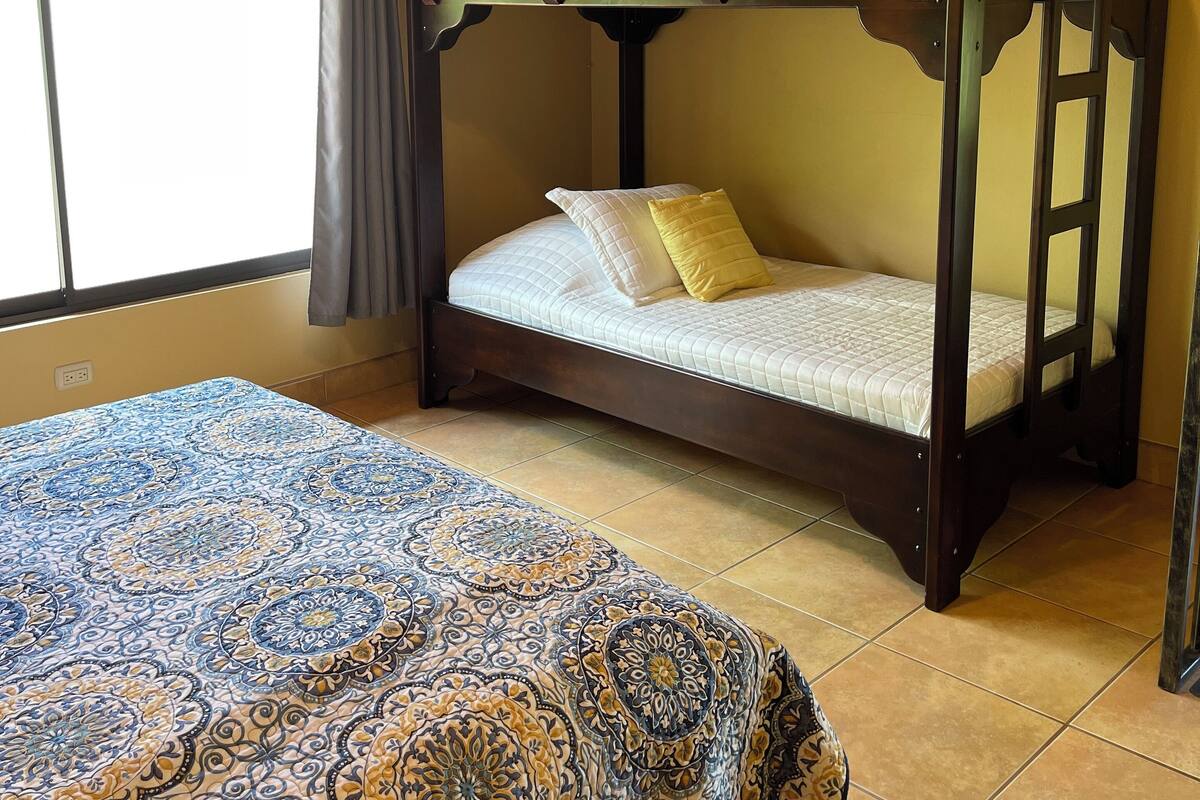 Una habitación con una litera, una colcha estampada y una ventana con cortinas.