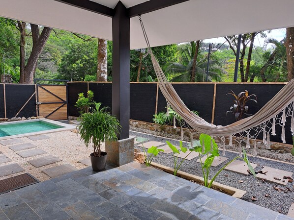 Un hamac, une petite piscine et des plantes en pot dans un espace aménagé en jardin.
