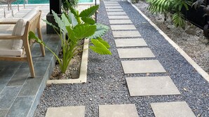 Un espace extérieur abrité comprenant une piscine, un hamac et un chemin en pierre.