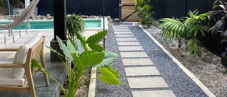 A covered outdoor area with a pool, a hammock, and a stone pathway.