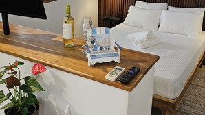Une chambre d’hôtel avec un lit, un bureau avec une télévision, une bouteille de vin, une télécommande et un panneau de bienvenue.