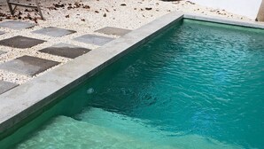 Une piscine à l’eau claire, bordée de carreaux et entourée d’un lit de galets.