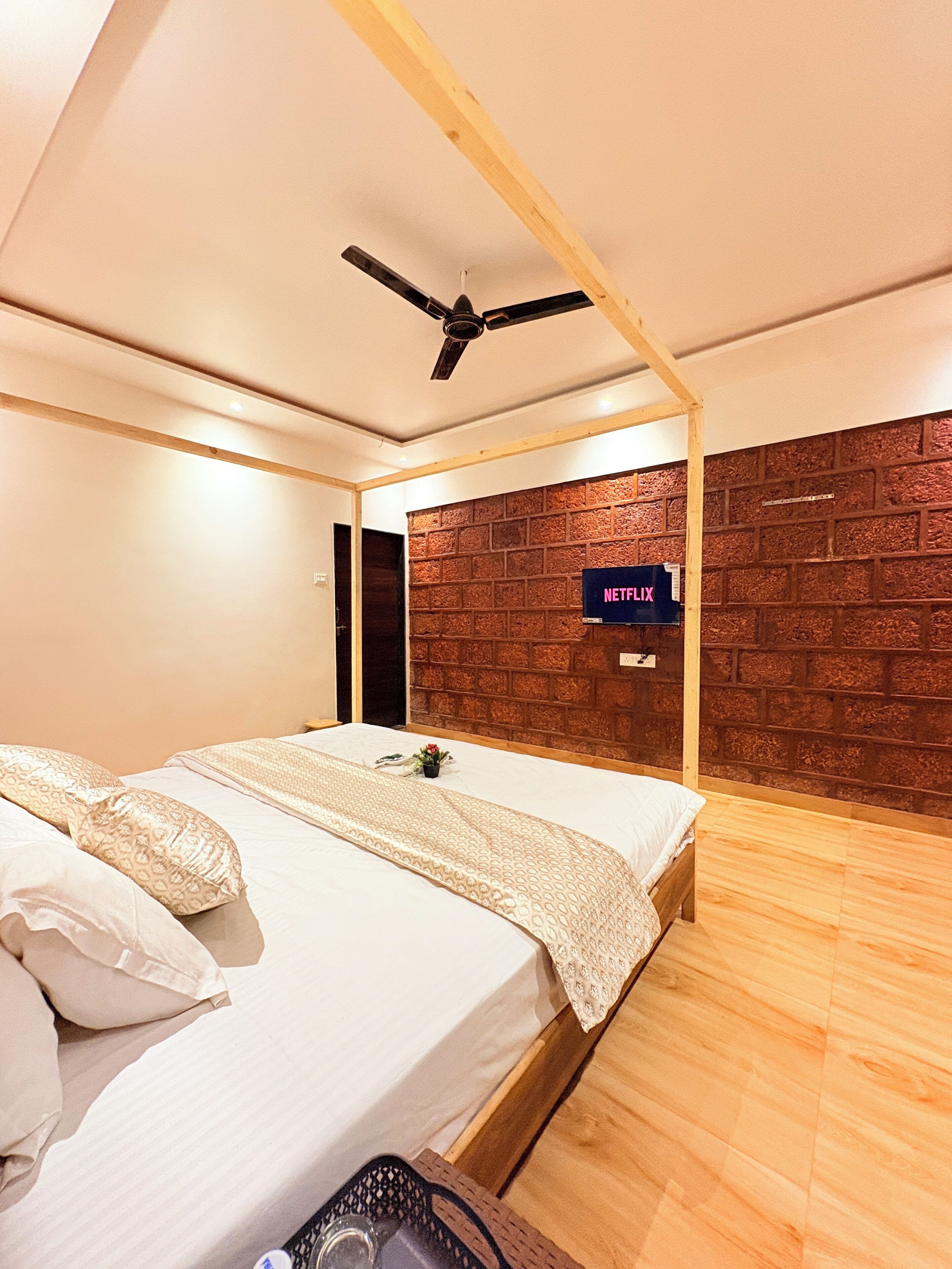 A modern bedroom with a wooden ceiling fan, a brick-patterned wall, and a mounted television displaying 'NETFLIX'.
