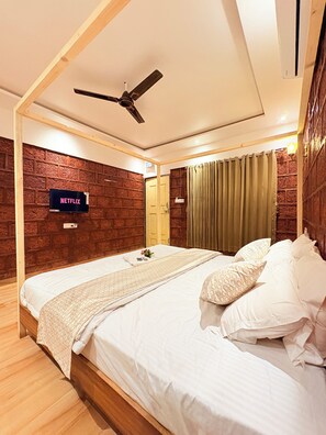 A bedroom with a wooden bed frame, a ceiling fan, a brick-patterned wall, and a mounted television displaying "NETFLIX". - Chardara Agro Tourism (Jaoli)