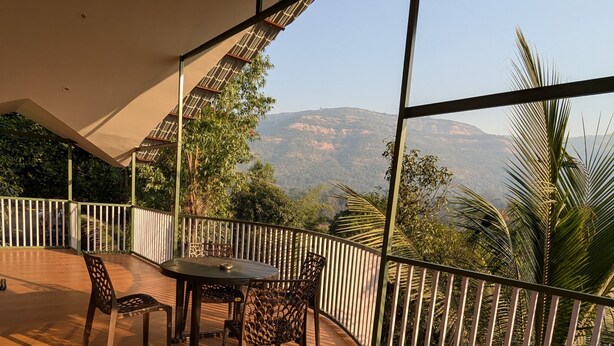 Uma área de estar coberta ao ar livre, com mesa e cadeiras, com vista para uma paisagem montanhosa.