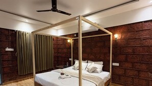 Uma cama com dossel sobre quatro pilares num quarto com soalho de madeira e paredes de tijolo.