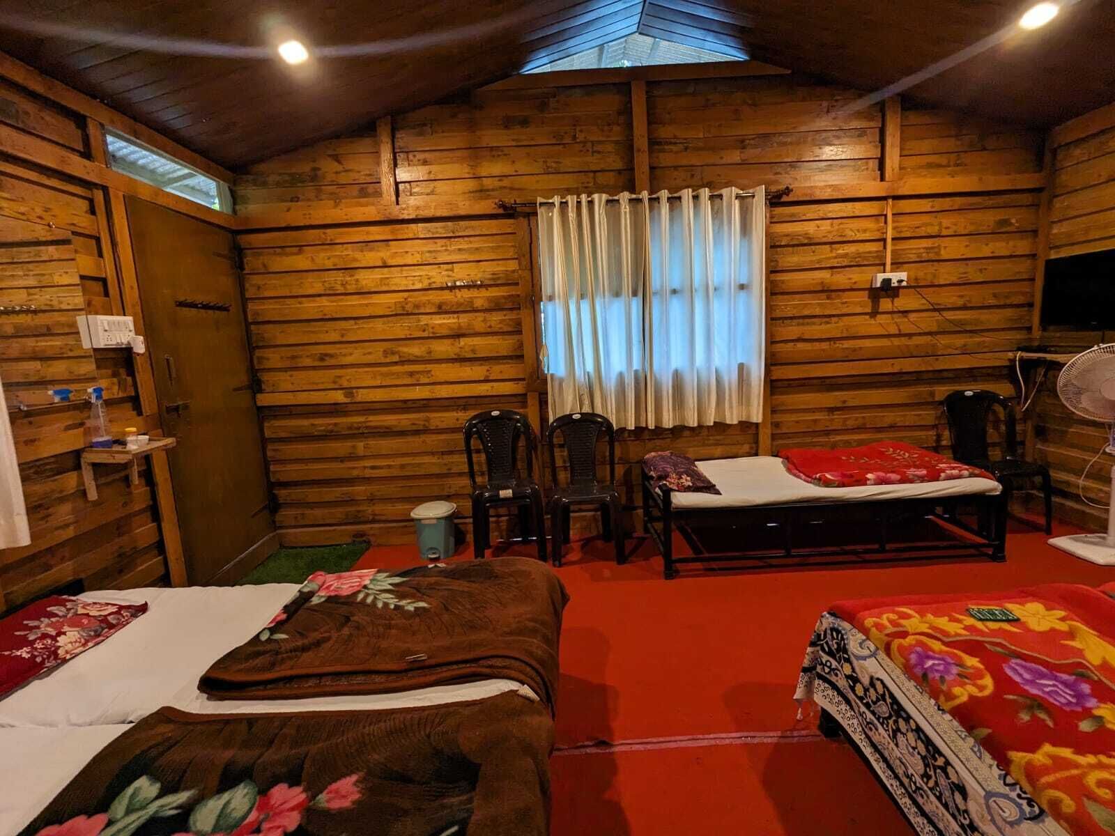 Habitación de cabaña de madera con dos camas, una mesita, una silla, un ventilador y una ventana con cortinas.