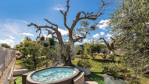 Een hottub omringd door groen en een boom.