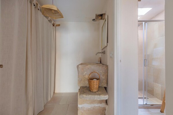 Un baño con lavabo de piedra, una cesta de madera y zona de ducha.