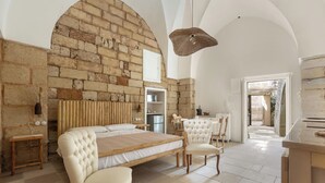 A spacious bedroom with a large bed, a wooden headboard, a brick wall, and a view of the outside.