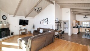 Ein geräumiges Wohnzimmer mit einem großen braunen Sofa, einem Kamin, einem Fernseher und einer Küchenzeile im Hintergrund.
