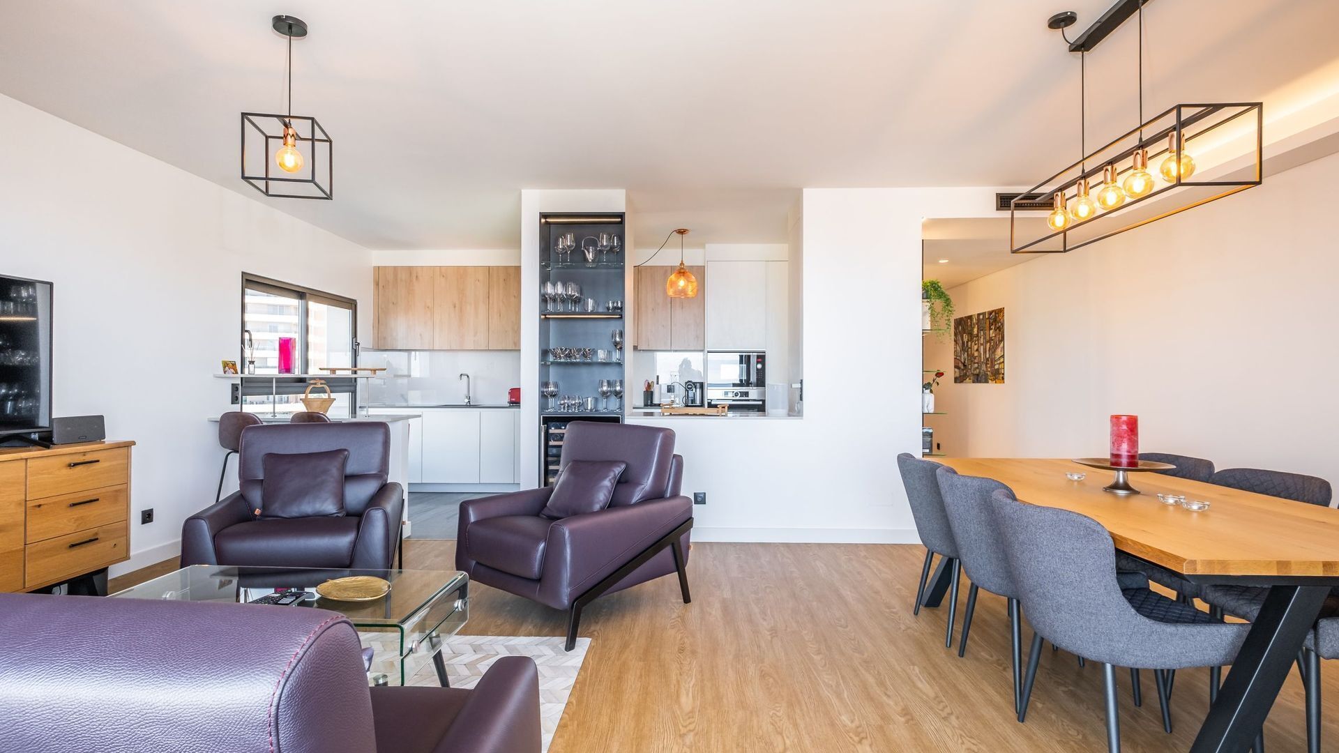 Un salon moderne avec des canapés en cuir, une table basse en verre et un coin repas comprenant une table en bois et des chaises grises.