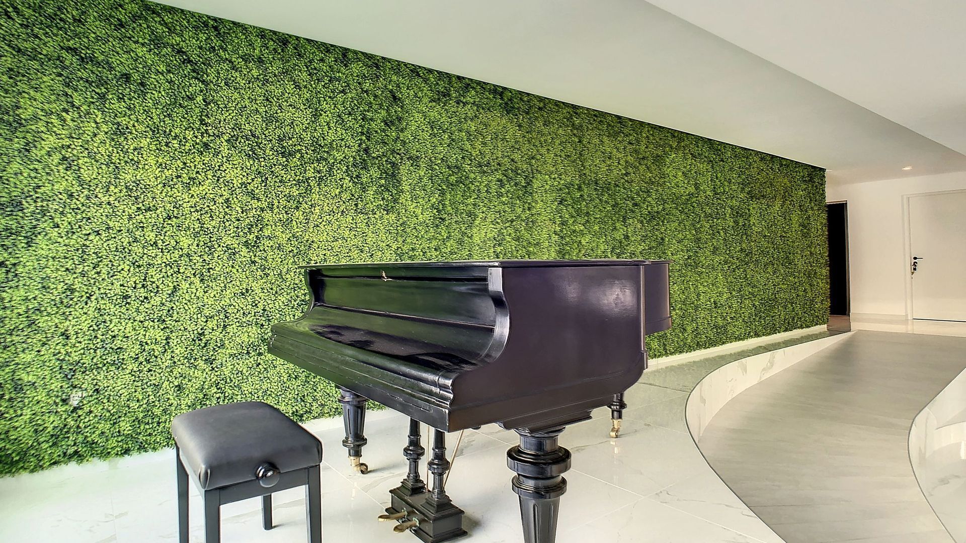 A grand piano in a modern lobby with a green wall and a curved floor.