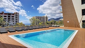A swimming pool with lounge chairs, surrounded by buildings and a mountainous backdrop. - SkyView Penthouse by LovelyStay (Funchal)
