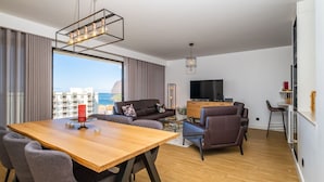 A modern living room with a wooden dining table, leather sofas, and a TV. - SkyView Penthouse by LovelyStay (Funchal)