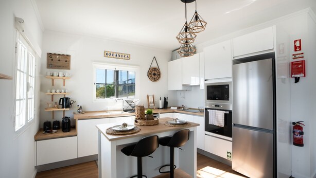 A modern kitchen with white cabinets, a central island with bar stools, a built-in oven, and a stainless steel refrigerator. - Ozeanica Heights by LovelyStay (Gaula)
