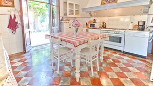 Une cuisine avec un carrelage à motifs, une table à manger avec des chaises, un lustre et une fenêtre donnant sur un paysage verdoyant.