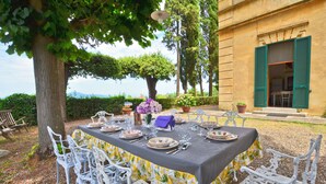 Un espace extérieur aménagé pour les repas, avec une table dressée pour quatre personnes, entourée de chaises blanches, devant un bâtiment aux volets verts.