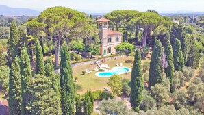 Une villa entourée de grands cyprès, dotée d’une piscine et d’une petite tour.