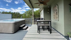 Un espace extérieur abrité comprenant un jacuzzi, une table et des chaises, un ventilateur de plafond et une fenêtre décorative.