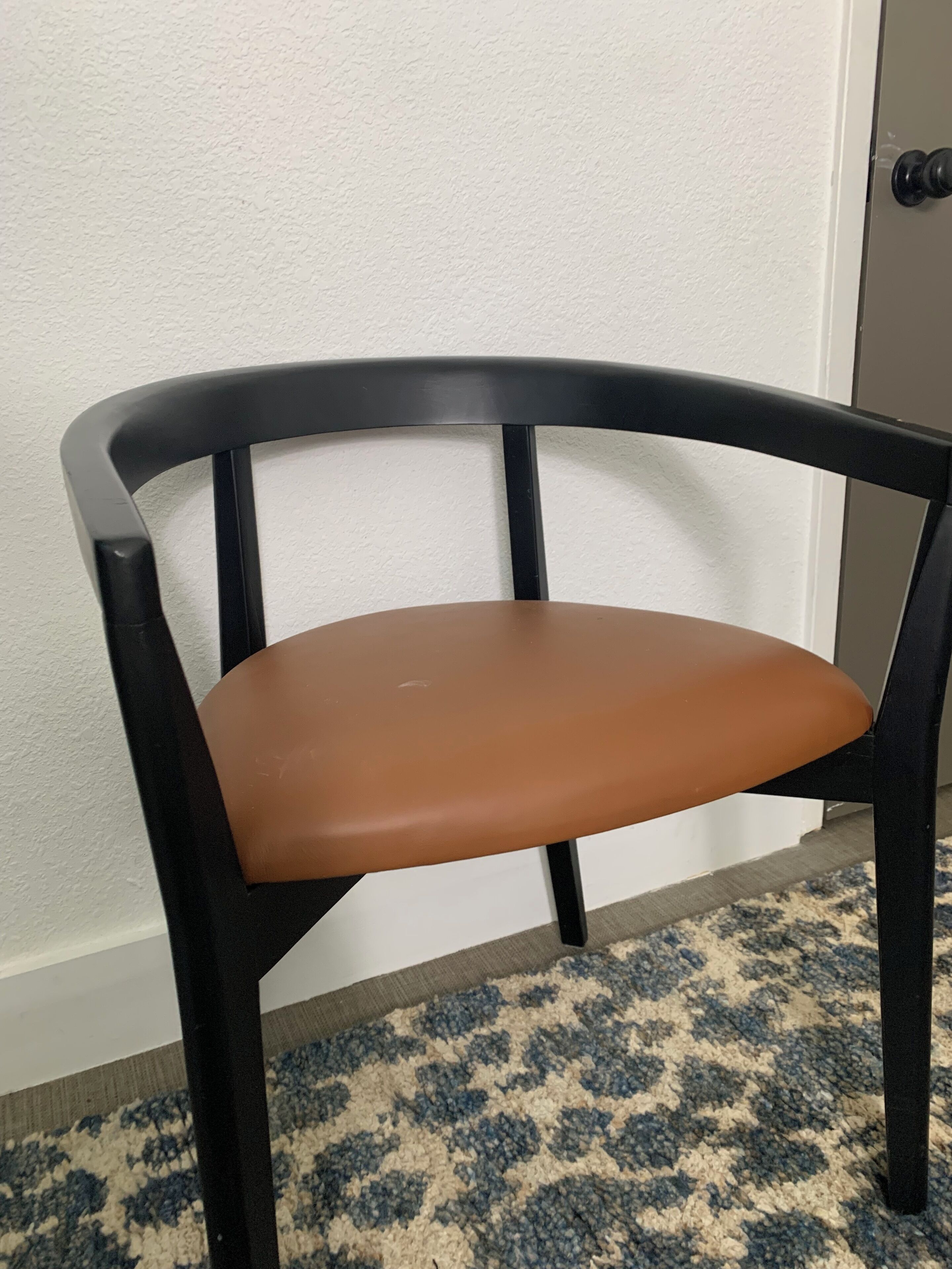 A chair with a curved backrest and a cushioned seat, positioned against a white wall with a textured surface.