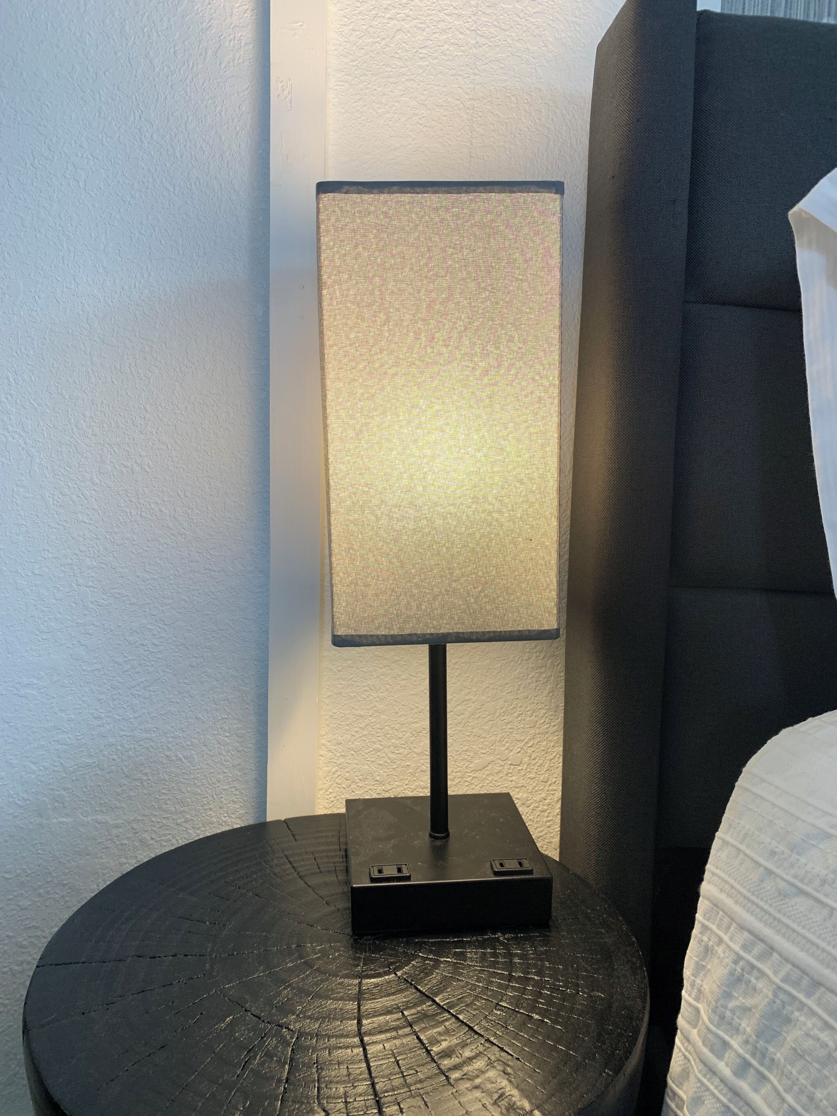 A nightstand with a lamp, a bed, and a wall.