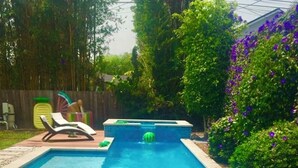 A rectangular swimming pool with a clear blue water surface, surrounded by a pebble border and a tiled deck area.
