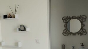 A modern bathroom with a white vanity, a mirror with an ornate frame, and a small shelf with a clock and decorative items. - Marie-France's comfort bungalow  (Baillif)