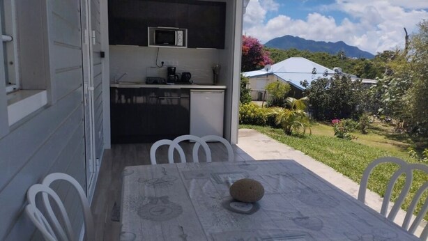 A dining area with a table and chairs, a stone on the table, and a kitchen in the background. - Marie-France's comfort bungalow  (Baillif)