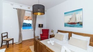 A hotel room with a wooden bed, a red chair, a small table, a lamp, and a painting of a sailboat on the wall. - Residence Villa Mima (Cavtat)