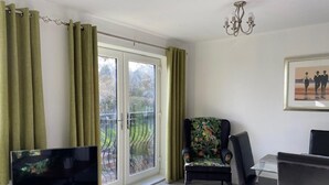 Uma sala de estar com televisão, uma mesa de jantar e uma cadeira estampada com flores.