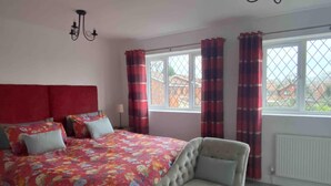 Quarto com uma cama grande, uma cadeira, uma janela com cortinas e um radiador.